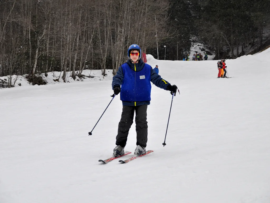 Skifahrer steht mit Stöcken auf der Piste am Waldrand.